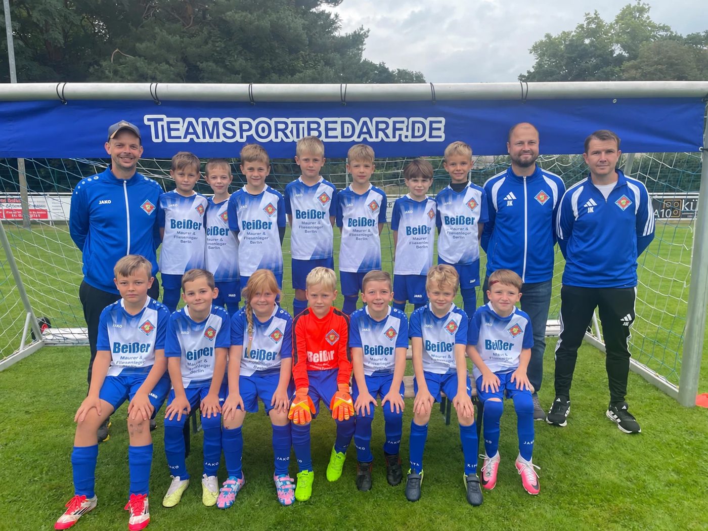 Mannschaftsfoto der F-Junioren der SG Aufbau Halbe: die Kinder in blau-weißen Trikots stehen und sitzen in zwei Reihen vor einem Fußballtor, vorn der Torwart in Rot, an den Seiten drei Trainer.