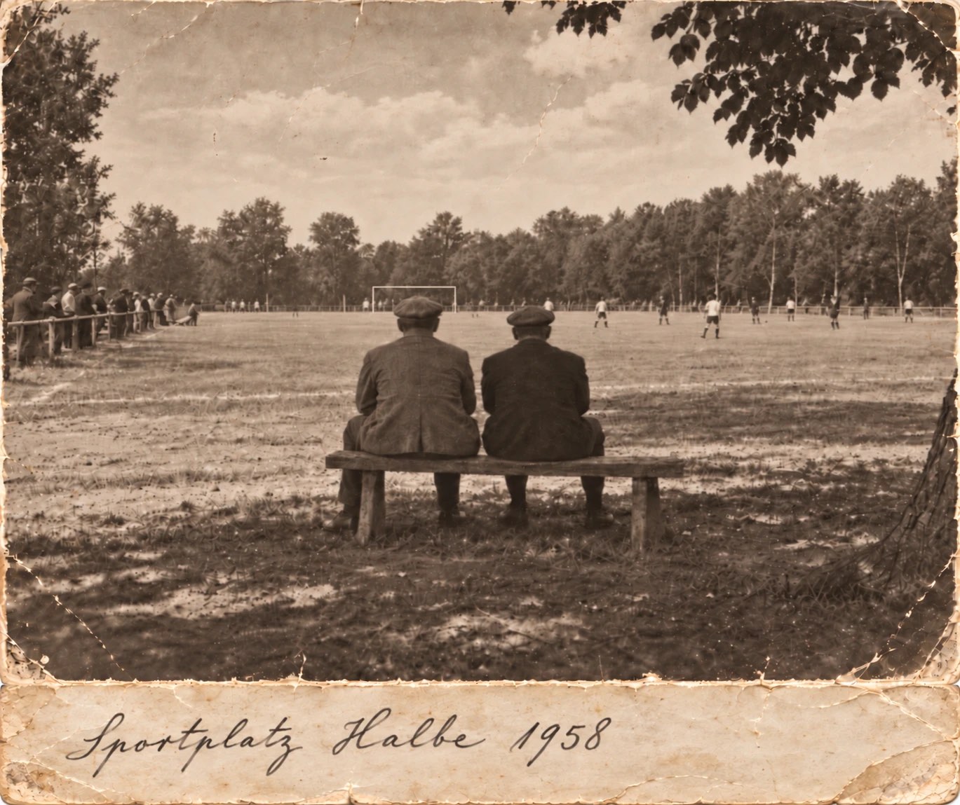 Historische Aufnahme vom Sportplatz Halbe: Zwei Männer mit Schiebermützen sitzen auf einer Holzbank und schauen einem Fußballspiel zu, am Spielfeldrand stehen Zuschauer. Handschriftliche Bildunterschrift auf dem Karton: „Sportplatz Halbe 1958“.