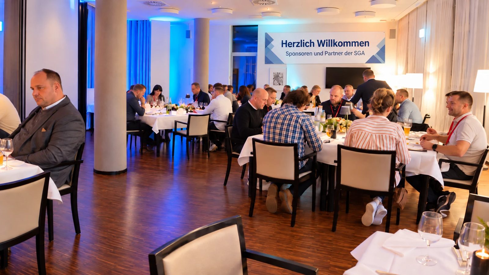 Gäste beim Tag der Sponsoren an festlich gedeckten Tischen, im Hintergrund ein Banner mit der Aufschrift „Herzlich Willkommen – Sponsoren und Partner der SGA“